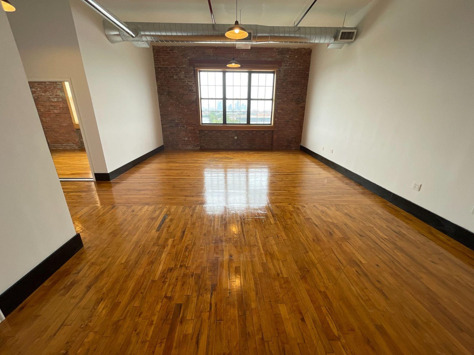 Unit 400 interior with restored hardwood floors, exposed brick wall and oversized window